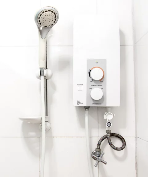 A wall-mounted electric water heater and shower in a white-tiled bathroom