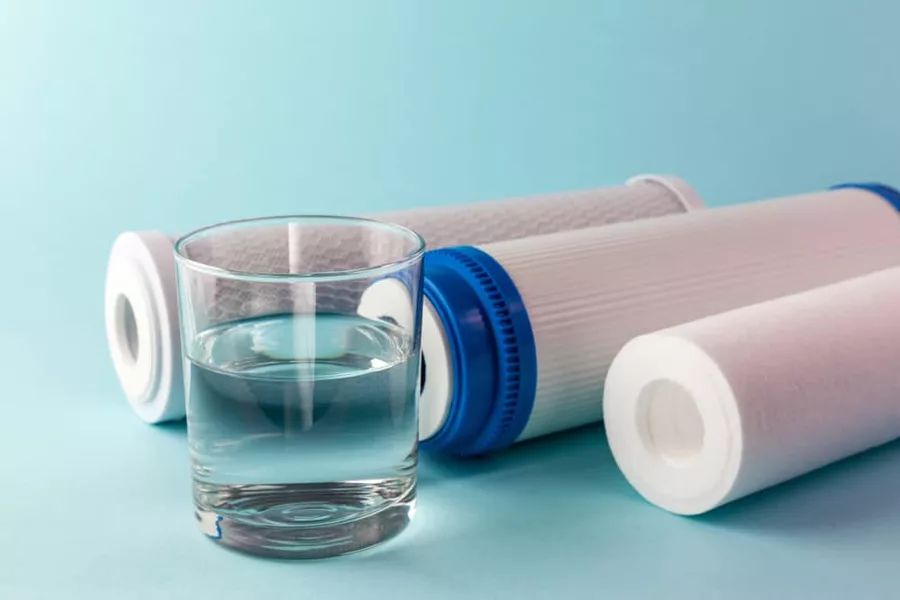 A glass of clear water in front of carbon filter cartridges
