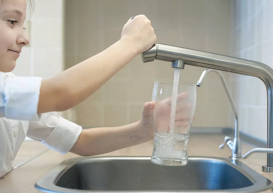 A child filling a glass with water from a kitchen tap